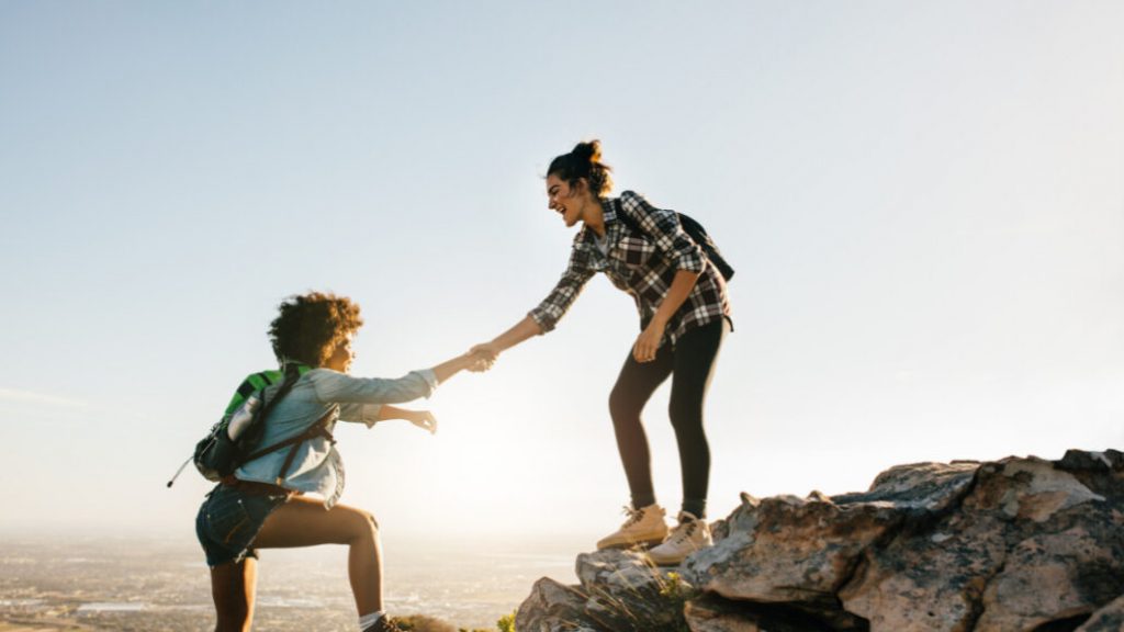 Two individuals standing on a mountain peak, united by holding hands, symbolizing companionship and triumph.