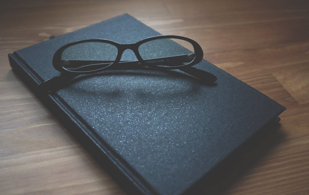 Glasses resting on a book atop a wooden table.