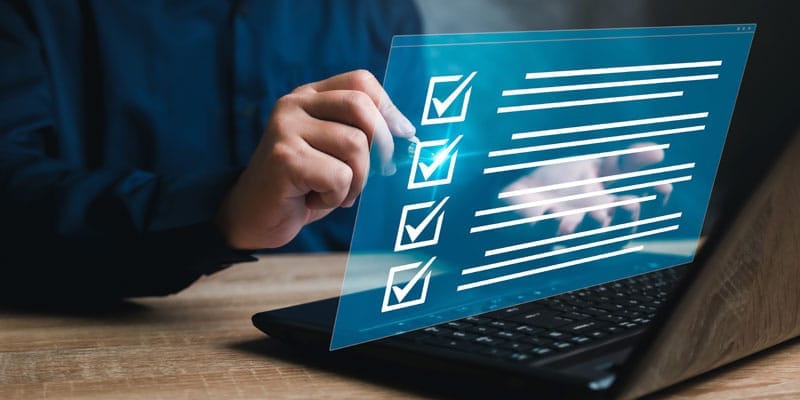 A man sitting at a desk, focused on his laptop screen, which displays a checklist.