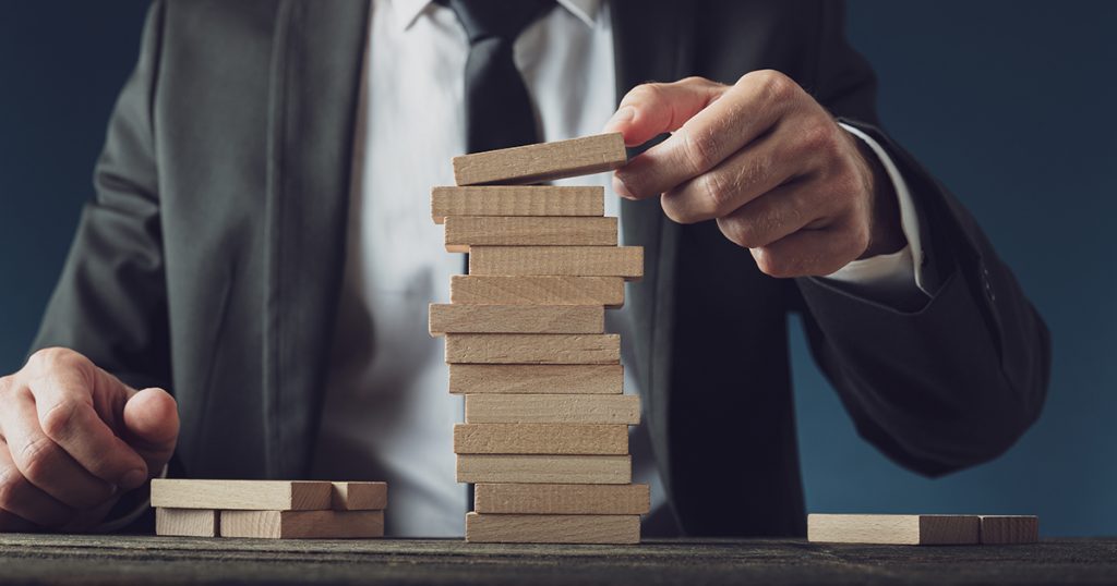 A professional man in formal attire carefully arranges wooden blocks on top of each other.