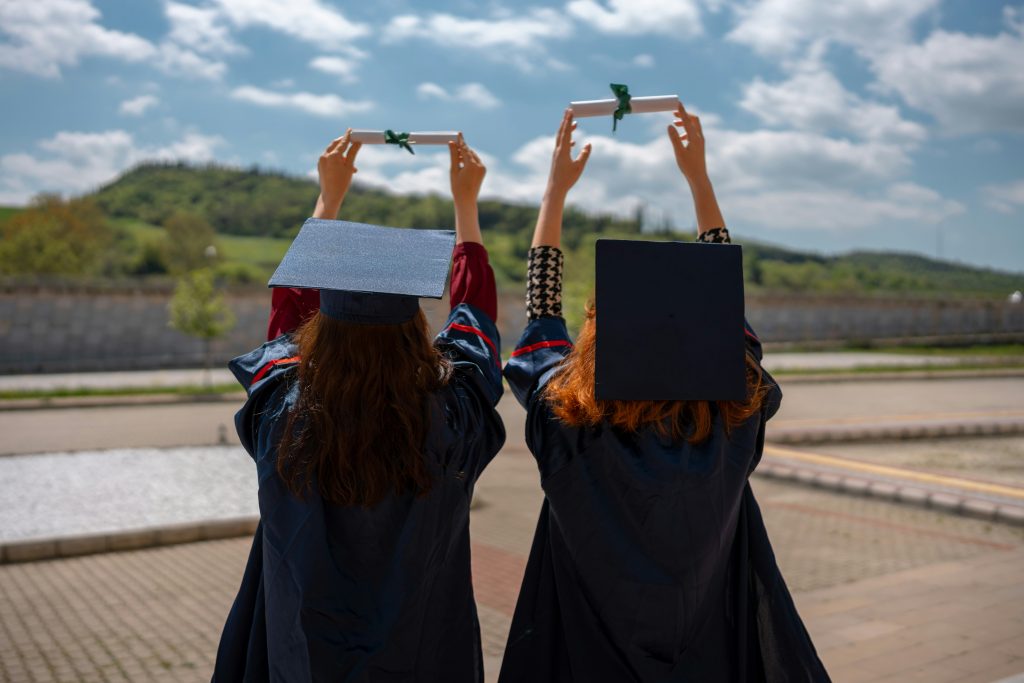 two women in graduation gowns holding diplomas