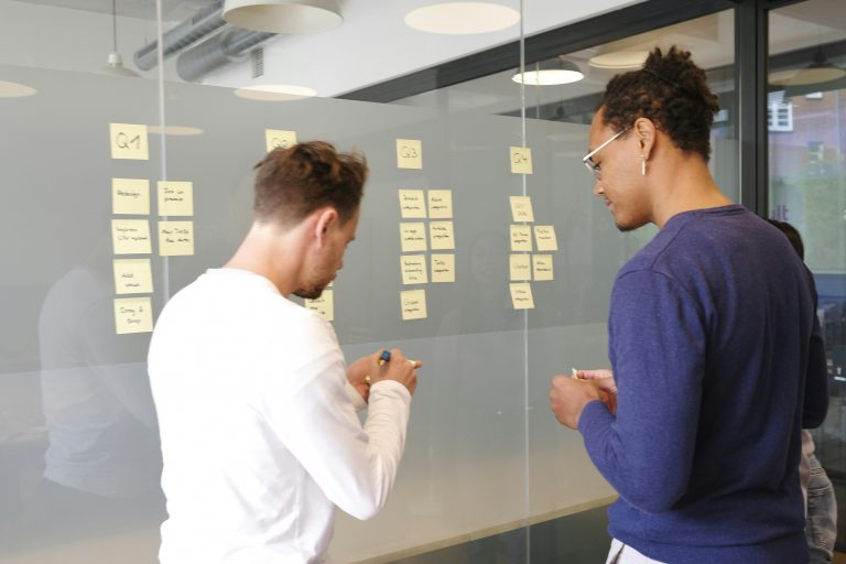 a couple of men looking at sticky notes on a glass wall