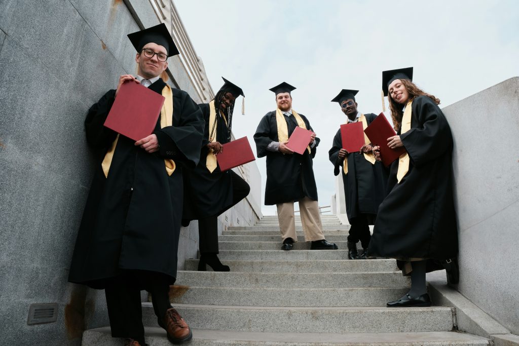 a group of people in graduation gowns and caps holding red papers