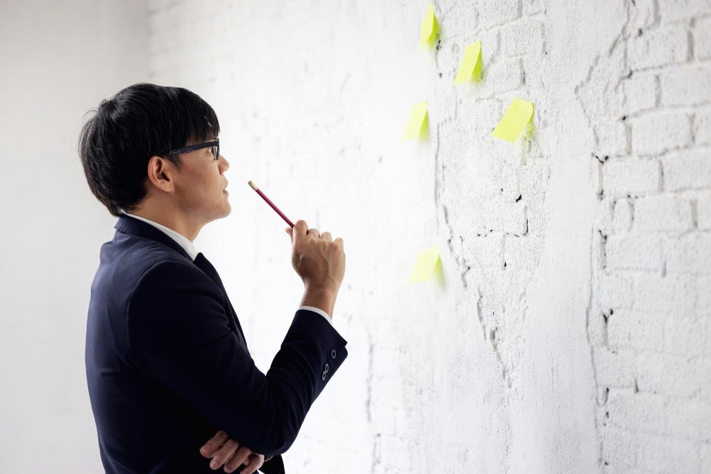 Expert Insights Into National Interest Waiver (NIW) Eligibility Criteria a man in a suit holding a pencil and looking at a wall with post-it notes