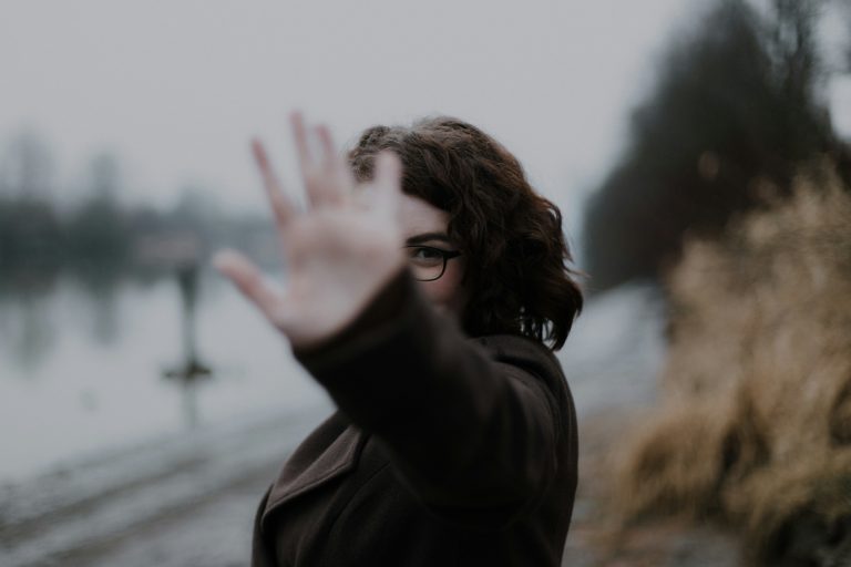 Person gesturing near a riverbank.