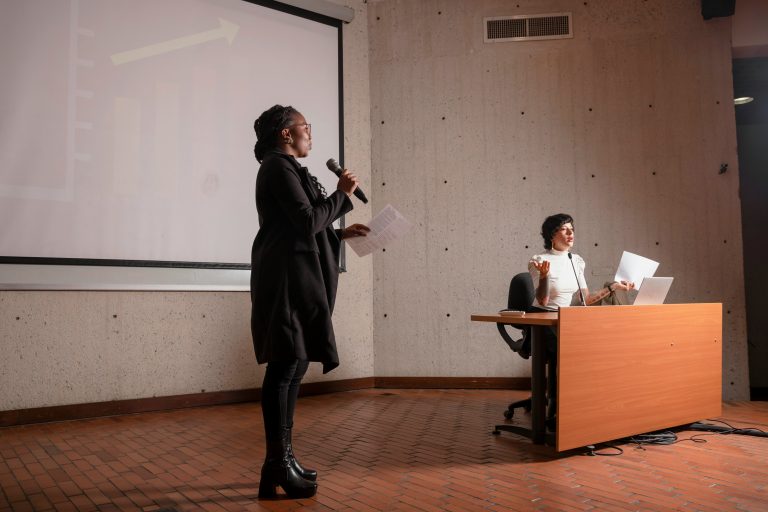 a woman standing in front of a desk holding a microphone