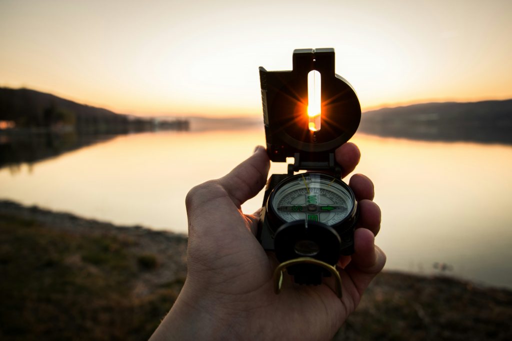 a hand holding a compass with a sunset in the background